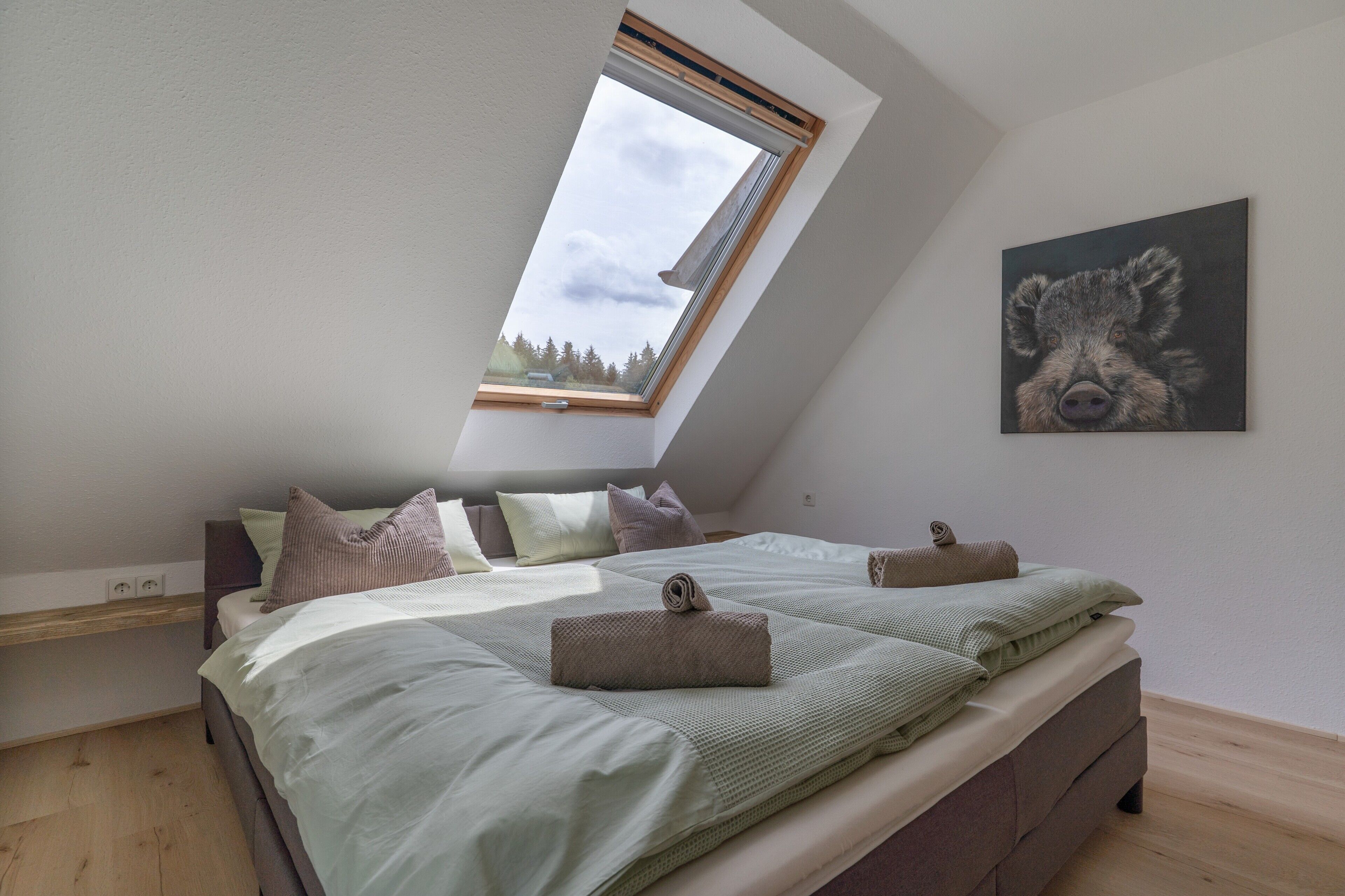 Une chambre avec un plafond en pente, un puits de lumière, un lit avec de nombreux oreillers et un tableau accroché au mur.