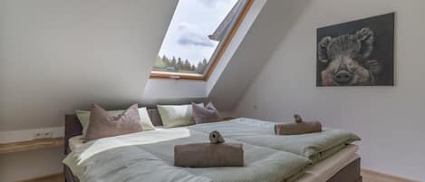 Une chambre avec un plafond en pente, un puits de lumière, un lit avec de nombreux oreillers et un tableau accroché au mur.