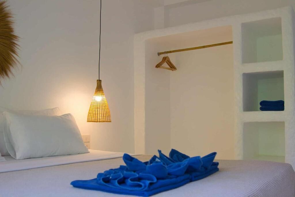 A hotel room with a bed, a hanging light fixture, a towel rack, and a shelf with folded towels.