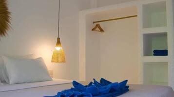 A hotel room with a bed, a hanging light fixture, a towel rack, and a shelf with folded towels.