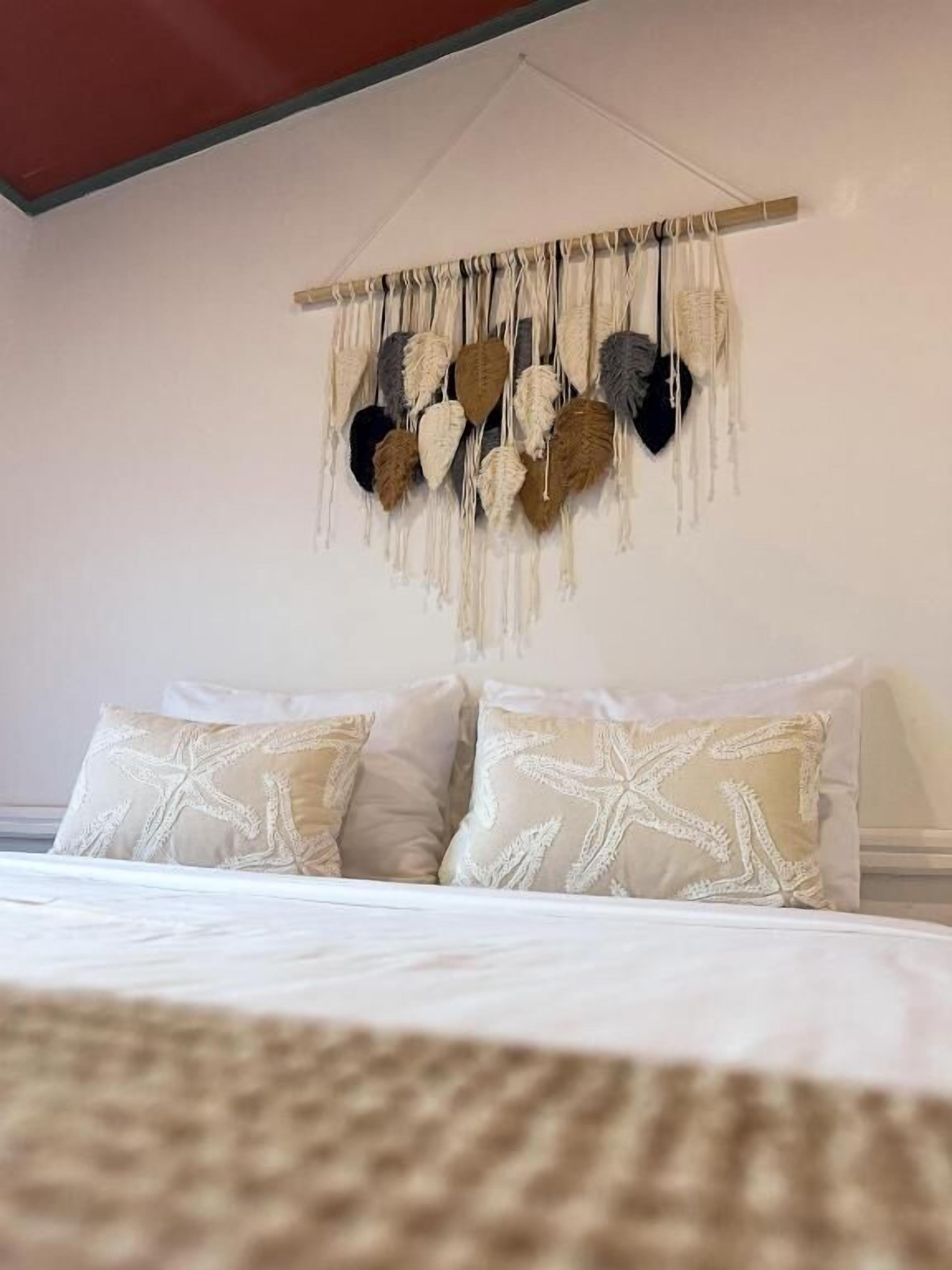 A bedroom with a bed, pillows, and a wall hanging.