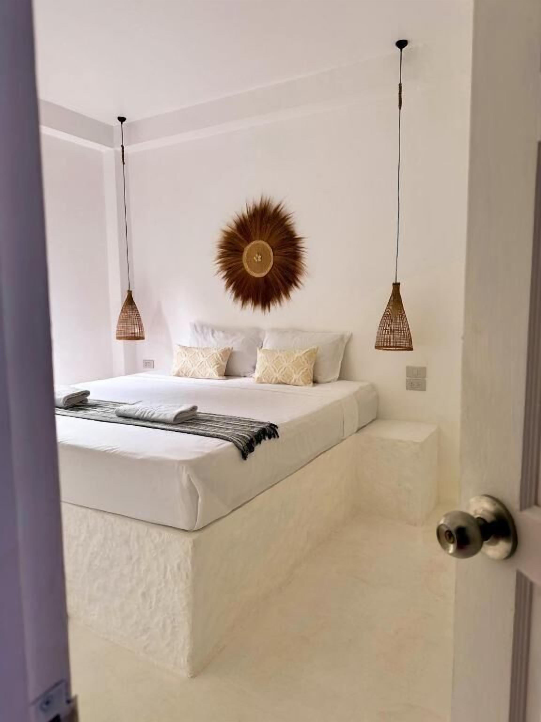 A bedroom with a bed, a wall-mounted sunburst decoration, and two hanging pendant lights.