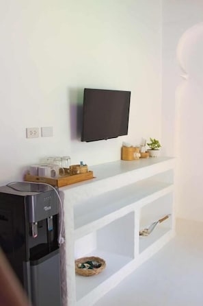 A modern kitchen with a built-in water dispenser, a flat-screen TV mounted on the wall, and a white countertop with a basket of bread. - Lanta Secret House (Saladan subdistrict)