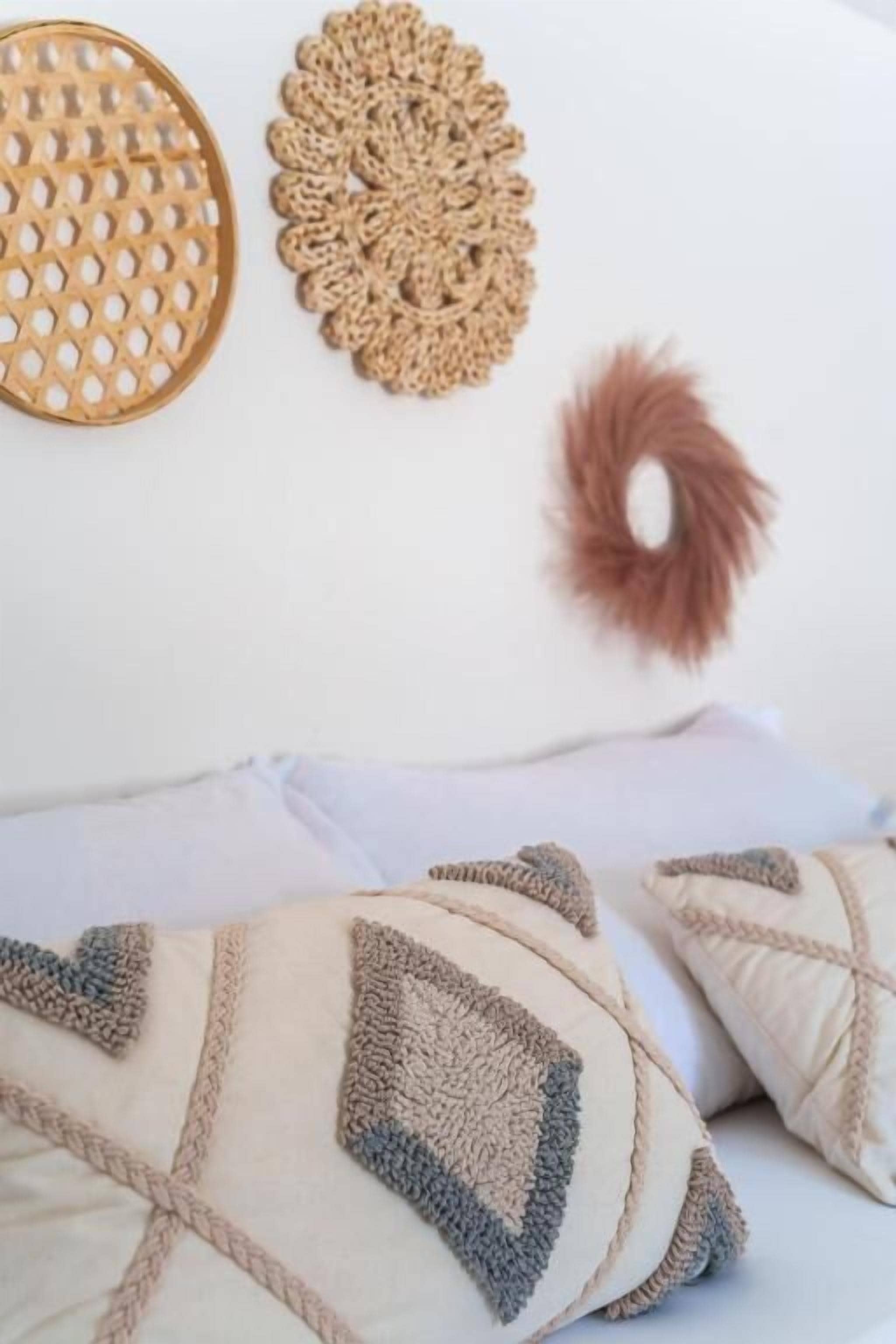 Ein Bett mit weißer Tagesdecke und zwei Kissen mit geometrischem Muster.
