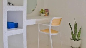 A room with a white desk, a chair, a potted plant, and a shelf with a mirror and a small decorative item.