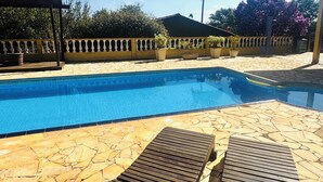 A swimming pool with a stone deck and wooden loungers.