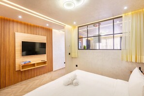 A modern hotel room with a large bed, a mounted TV, wooden paneling, and a window with curtains. - 1-bedroom apartment in charming Marrakech with AC (Marrakech)