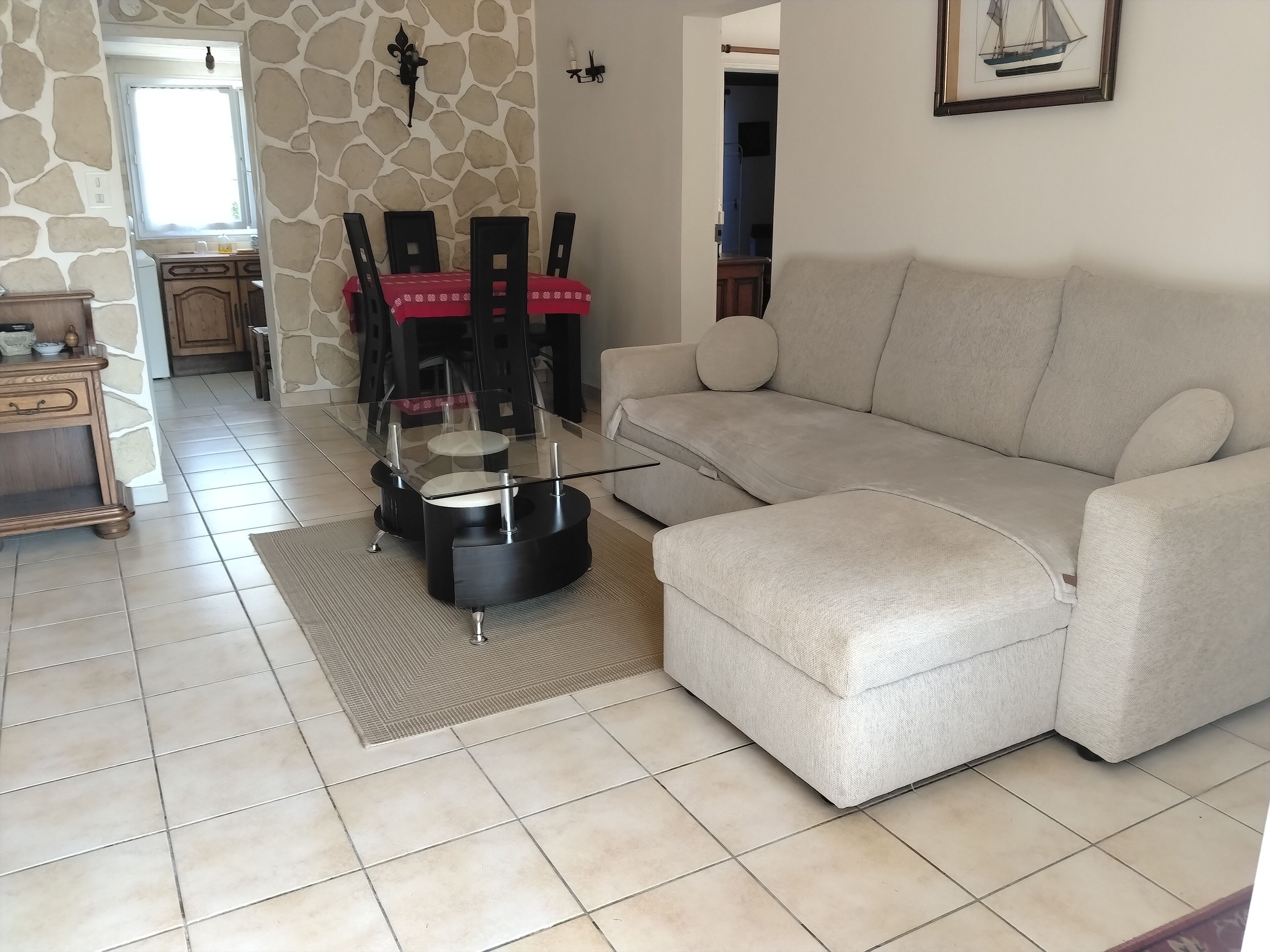 A living room with a beige sofa, a glass coffee table, and a dining area with a red tablecloth.
