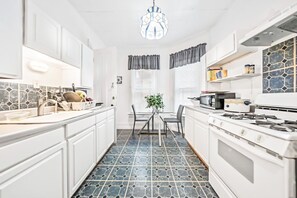 A modern kitchen with white cabinetry, a gas stove, a microwave, and a dining area with a table and chairs.