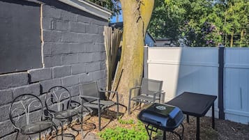 A patio area with a grill, metal chairs, and a table.