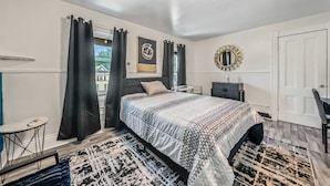 A bedroom with a bed, a bedside table, a dresser, a mirror, and a view of the outside.