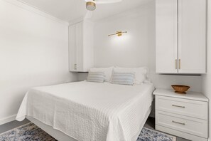 Ein Schlafzimmer mit Bett, weißem Kleiderschrank, Nachttisch und Deckenventilator.