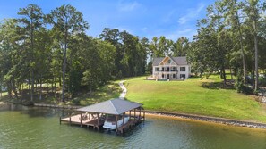 A lakeside property with a dock, a house with a large lawn, and a forested area. - Lake Sinclair Dream Home w/ Everything|Pool|HotTub (Milledgeville)