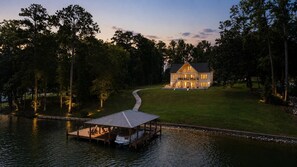 A lakeside property with a dock, a covered boat house, and a large house with multiple windows.