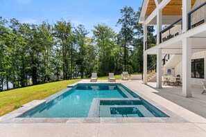 A swimming pool with a deck, surrounded by trees and a building with outdoor seating.
