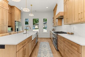 A modern kitchen with wooden cabinets, a white countertop, stainless steel appliances, and pendant lighting.