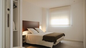 A bedroom with a bed, bedside table, and a window with blinds. - Almar Suites Daimús (Daimús)