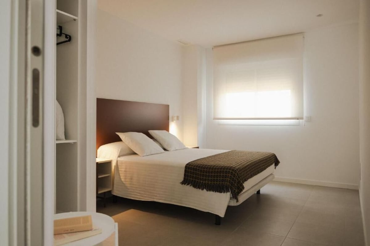 Ein Schlafzimmer mit Bett, Nachttisch und einem Fenster mit Jalousien.