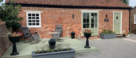 A brick house with a tiled roof, a green door, and a patio with outdoor furniture.