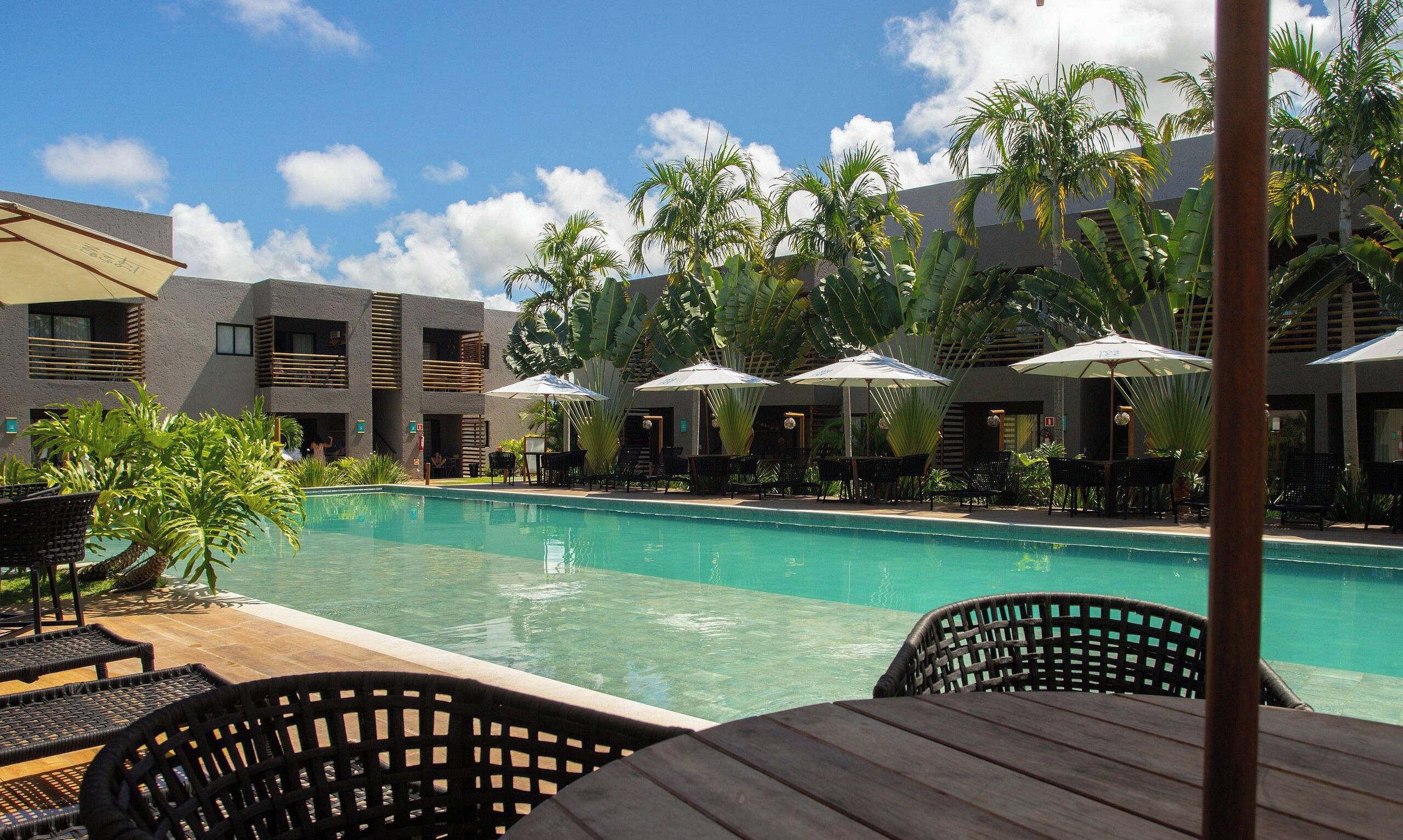 A pool area with lounge chairs and umbrellas, surrounded by palm trees and modern buildings.