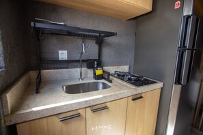 Une cuisine de taille réduite, dotée d’un évier en acier inoxydable, d’une cuisinière à gaz et d’un réfrigérateur noir.