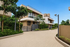 Un edificio residencial moderno con un sendero pavimentado, rodeado de vegetación y un cielo despejado.