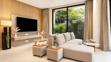 A modern living room with a large flat-screen TV, a sectional sofa, a coffee table, and a side table with books.