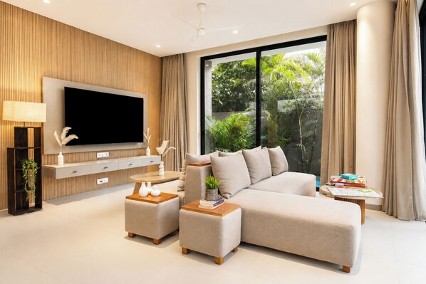 Una sala moderna con un televisor de pantalla plana grande, un sofá modular, una mesa de centro y una mesita de noche con libros.