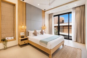 A modern hotel room with a large bed, wooden headboard, bedside lamps, a nightstand, and a view of the outside through a large window.