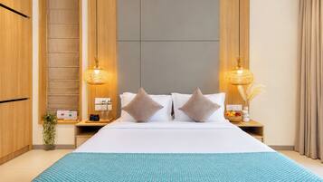 A hotel room with a large bed, two bedside lamps, a nightstand with a fruit bowl, and a wooden wardrobe.