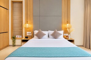 Una habitación de hotel con una cama grande, dos lámparas de noche, una mesita de noche con un frutero y un armario de madera.