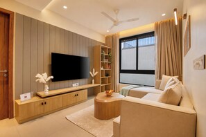 Una sala de estar moderna con televisor de pantalla plana, muebles de madera, una estantería y un ventanal con cortinas.