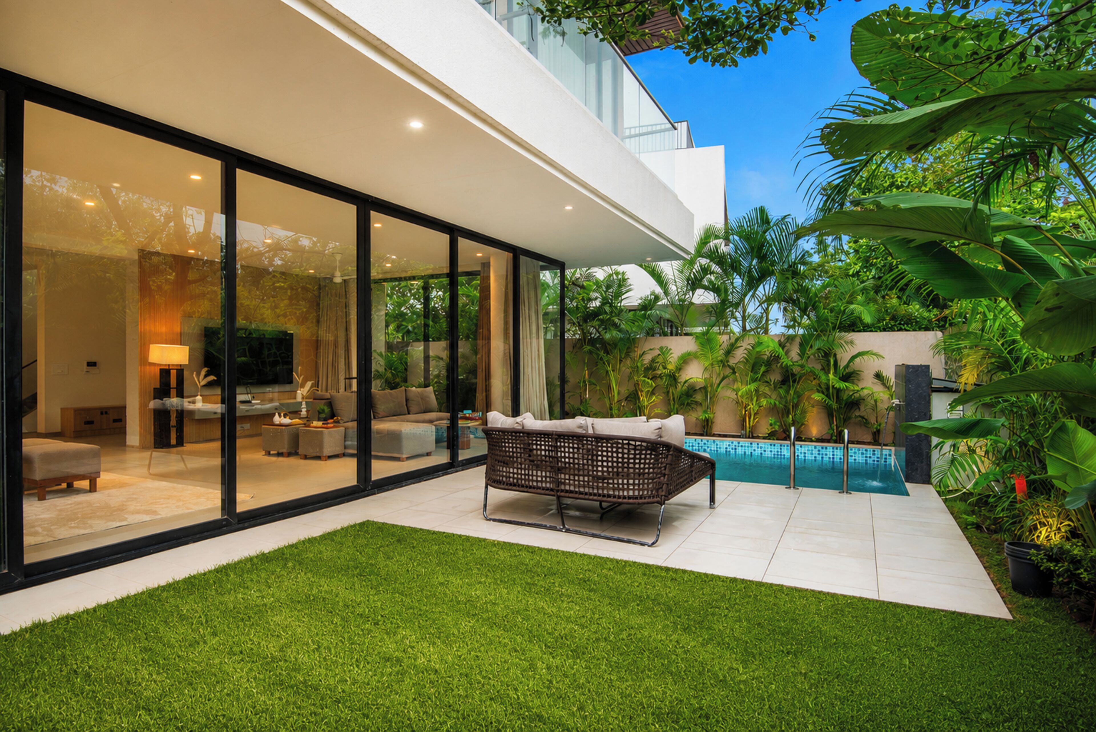 A modern house with a glass facade, a swimming pool, and a well-maintained lawn.