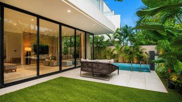 A modern house with a glass facade, a swimming pool, and a well-maintained lawn.