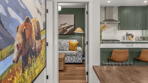 Eine moderne Küche mit grünen Schränken, ein Essbereich mit Holztisch und ein Wohnzimmer mit Sofa und Gemälde.