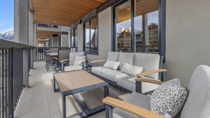 Ein moderner Außenbereich mit einer Couch, Stühlen und einem Tisch mit Blick auf eine gebirgige Landschaft.
