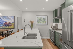 A modern kitchen with a marble countertop, stainless steel appliances, and a dining area with a wooden table and chairs. - Modern 4BR|Hot Tub and Mountain Views|Steps from Downtown (Canmore)