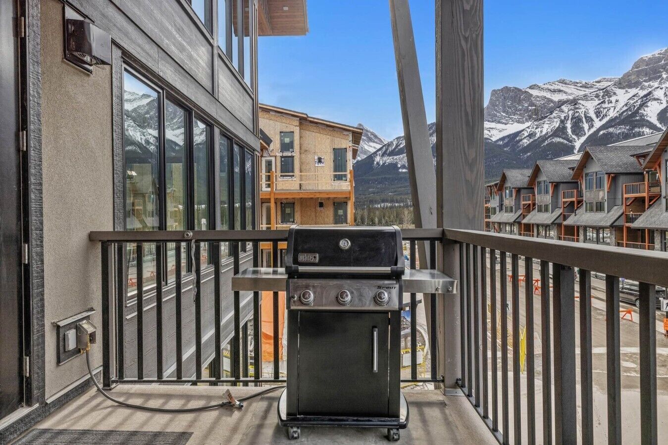 A balcony with a grill, overlooking a mountain landscape and neighboring buildings.