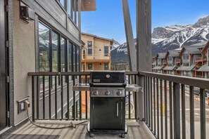 A balcony with a grill, overlooking a mountain landscape and neighboring buildings. - Modern 4BR|Hot Tub and Mountain Views|Steps from Downtown (Canmore)