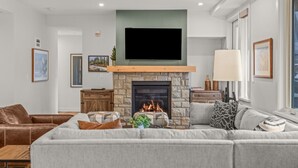 Ein modernes Wohnzimmer mit Kamin aus Stein, einem flachbildfernseher darüber und einem großen, grauen Sofa.
