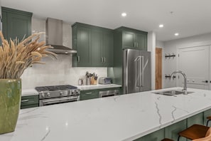 A modern kitchen with green cabinets, stainless steel appliances, and a marble countertop. - Modern 4BR|Hot Tub and Mountain Views|Steps from Downtown (Canmore)