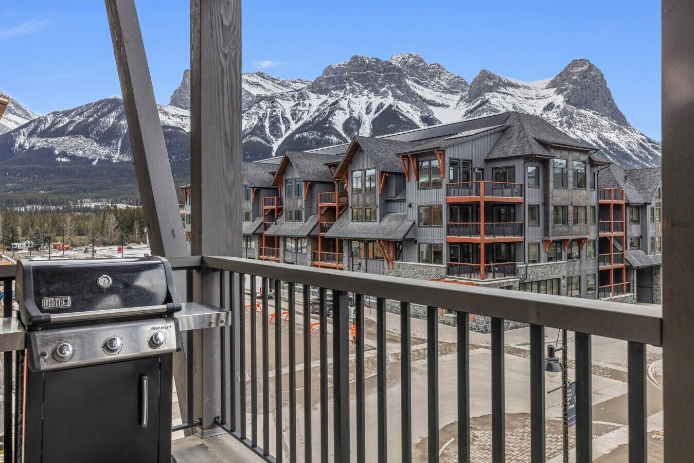 A balcony with a Weber Spirit grill, overlooking a modern building with multiple balconies and a mountainous backdrop.