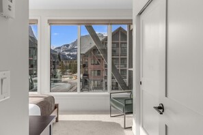 A bedroom with a large window, a bed, a chair, and a door. - Modern 4BR|Hot Tub and Mountain Views|Steps from Downtown (Canmore)