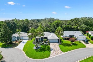 A residential area with houses, a curved driveway, and a well-maintained lawn. - Oasis in the Sun - tropical retreat w/ 4-seater golf cart (The Villages)