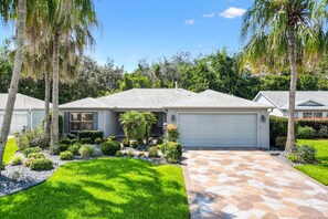 A residential house with a garage, surrounded by well-maintained landscaping and palm trees. - Oasis in the Sun - tropical retreat w/ 4-seater golf cart (The Villages)