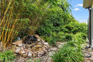 Um jardim com uma pequena cascata, bambu denso e diversos arbustos.
