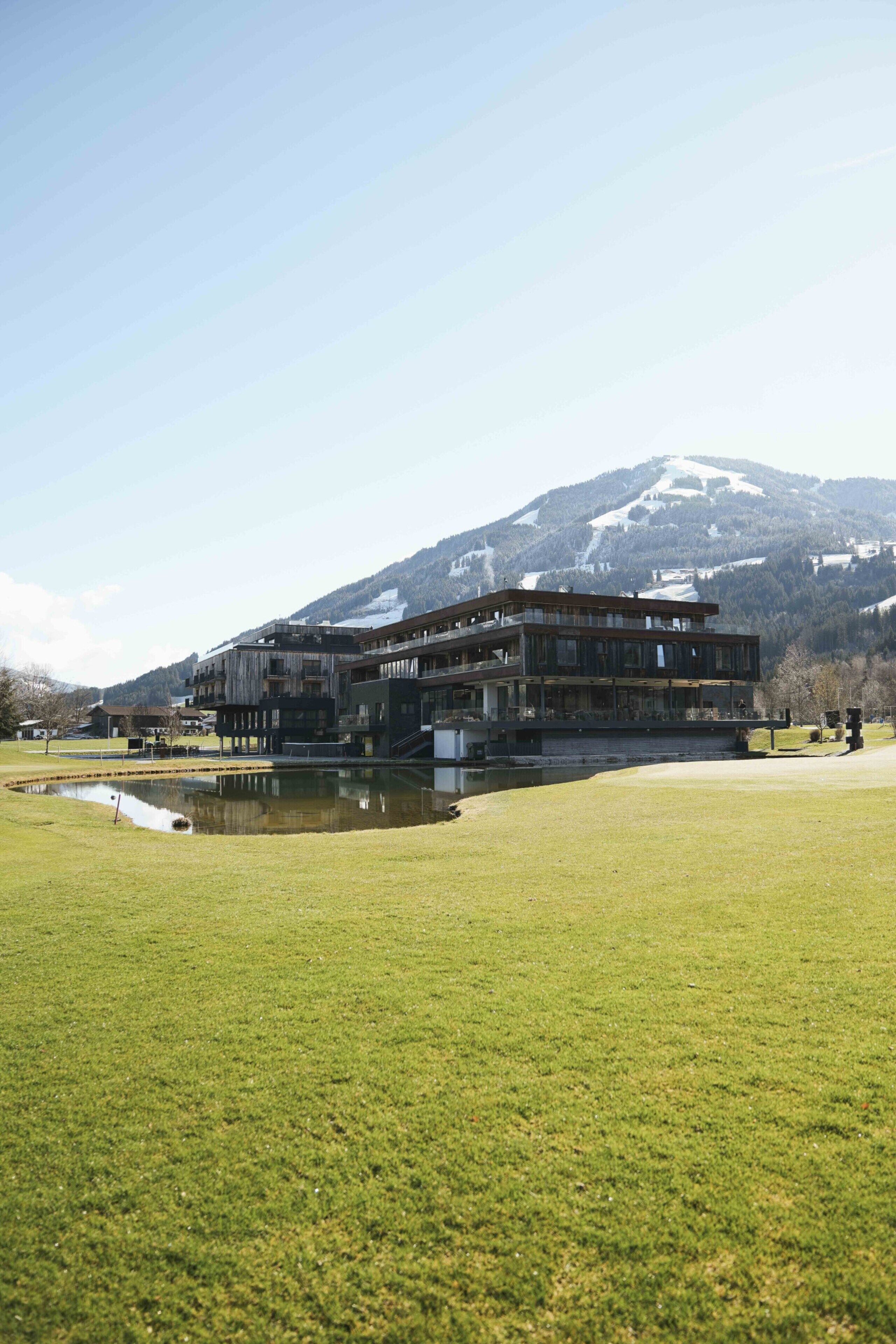 A modern building with a glass facade, situated in a grassy area with a mountain in the background.