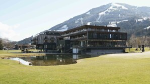 A modern building with a glass facade, situated in a grassy area with a mountain in the background. - Apartment mit 2 Schlafzimmern (Westendorf)