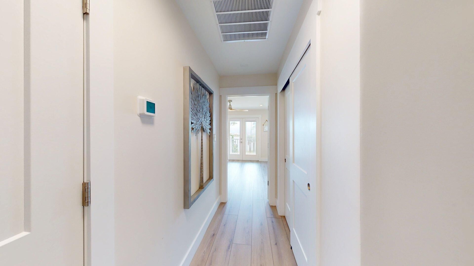 A hallway with a ceiling vent, a door on the left, and a door at the end.