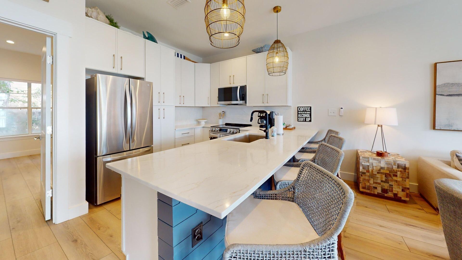 A modern kitchen with a central island, stainless steel appliances, and a seating area with wicker chairs.